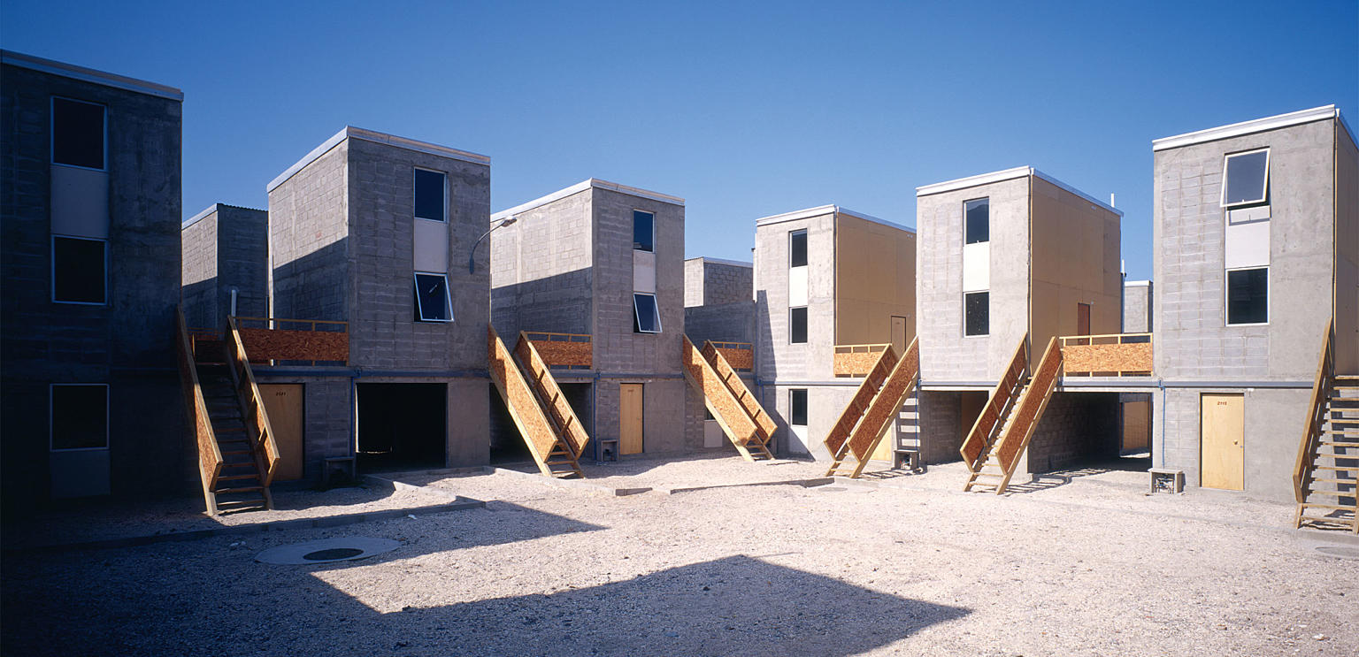 Boligområde med 93 enheter i Iquique i Chile, tegnet av arkitektene i Elemental og bygget i 2004. Bare halve huset bygges – resten må beboerne bygge selv. 36 kvm bolig kan utvides til 70 kvm. Duplex på 25 kvm kan utvides til 73 kvm. Byggherre: Chile Barrio.
