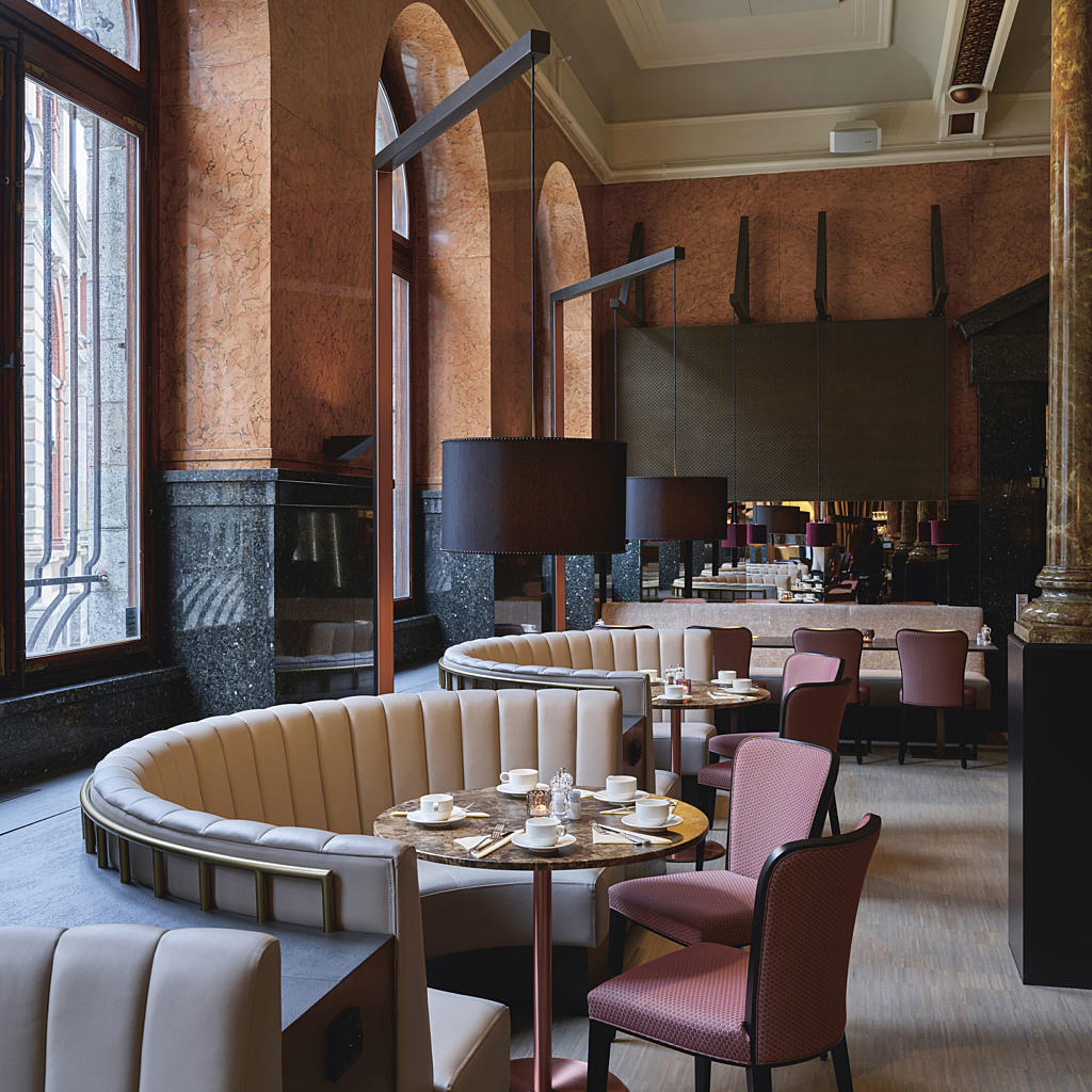 Buede sofaalkover bølger seg mellom innside yttervegg og runde bord. Laserskårne akustikkpanel og stativ til nedhengte lamper matcher den sterke arkitekturen i rommet.