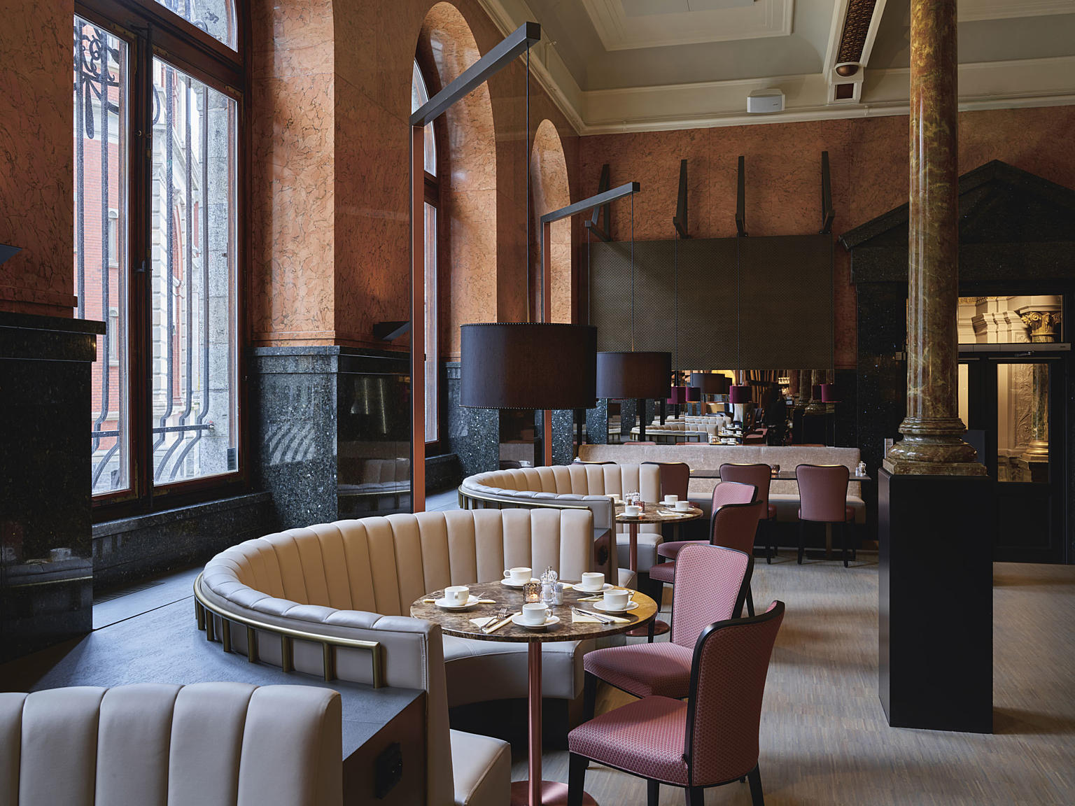 Buede sofaalkover bølger seg mellom innside yttervegg og runde bord. Laserskårne akustikkpanel og stativ til nedhengte lamper matcher den sterke arkitekturen i rommet.