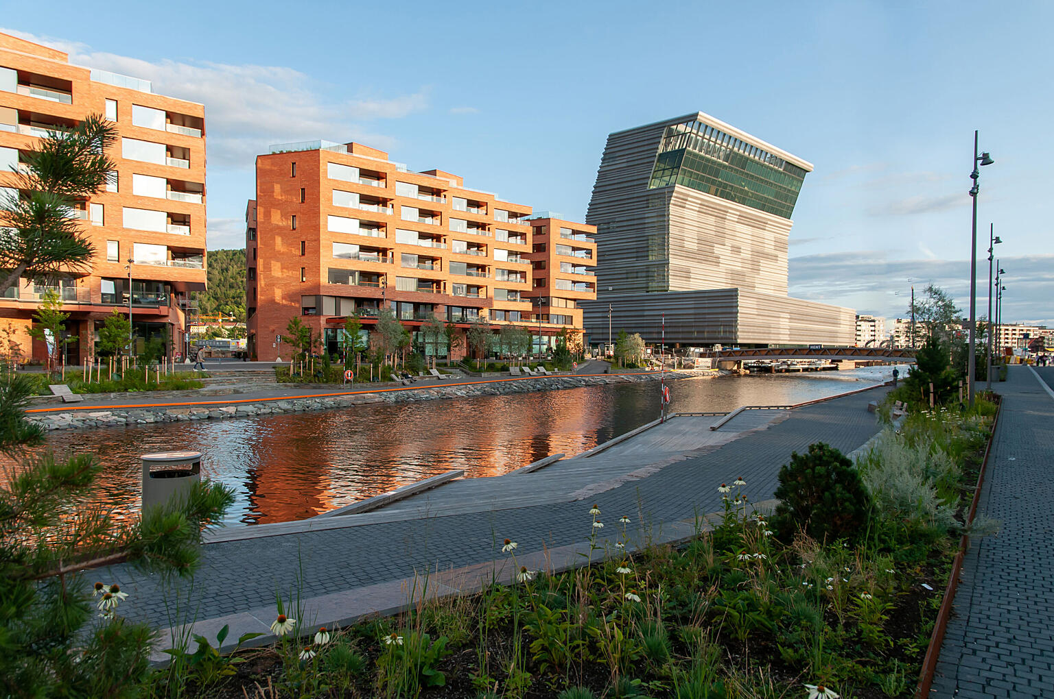 Det frodige byrommet langs Akerselvas utløp berikes ytterligere av den tydelige kontrasten i farge og materialitet mellom det nye boligkvartalet og det nye Munchmuseet.